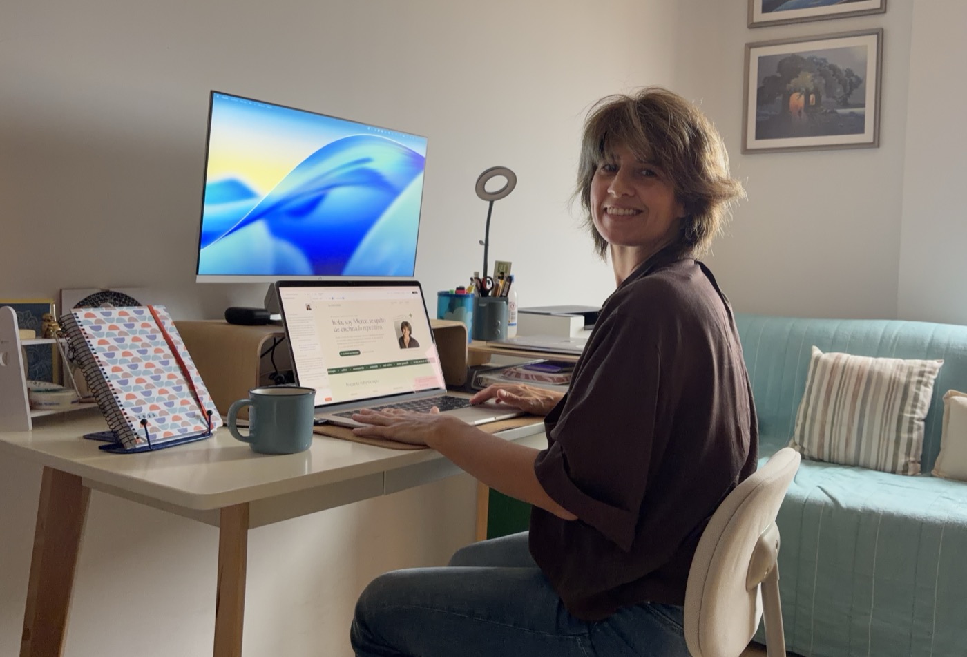 Merce sonriendo en su mesa de trabajo, con esta web abierta en el portátil